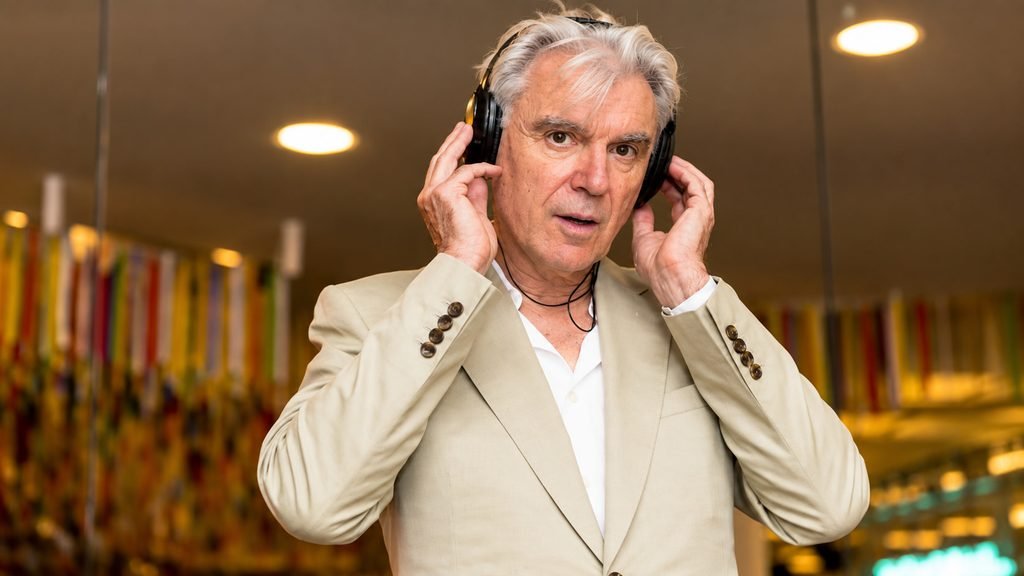 David Byrne wearing headphones and a beige suit