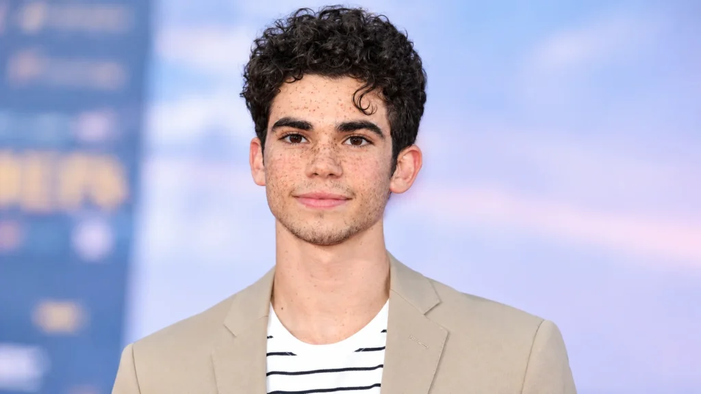 Cameron Boyce wearing a tan blazer and striped shirt in a professional portrait