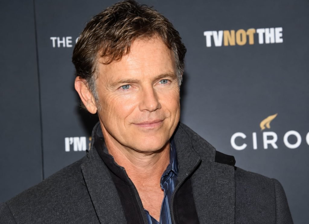 Bruce Greenwood smiling at a red-carpet event in a dark coat