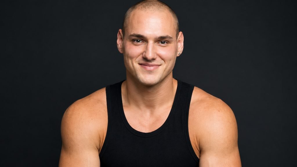 Leo Skepi wearing a black tank top against a dark background
