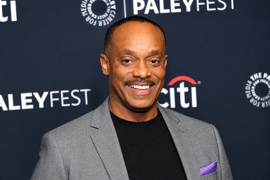 Rocky Carroll smiling in a gray blazer and black shirt at a PaleyFest event